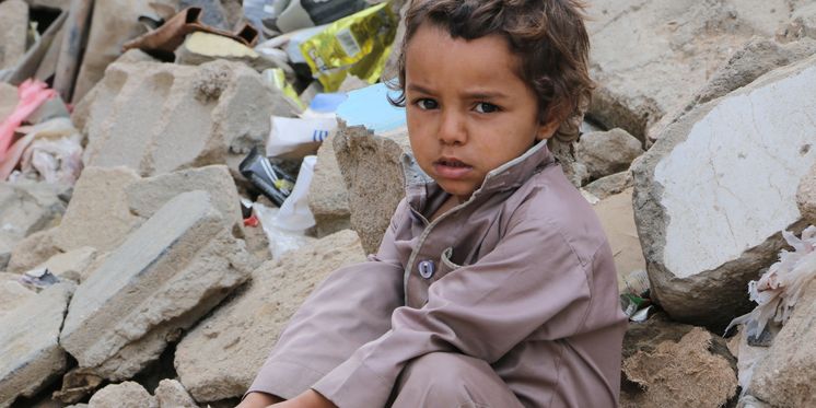 Kind sitzt auf Trümmern